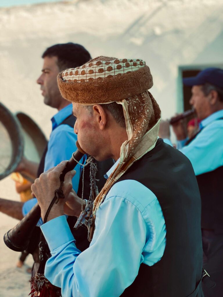 Musicians in traditional attire playing wind instruments outdoors at a cultural festival.
