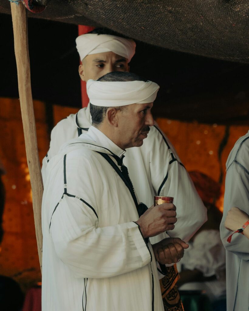 Two Moroccan men in traditional attire participate in a cultural gathering.
